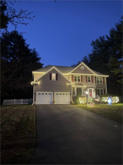 Colonial home outlined in warm white Christmas lights at dusk