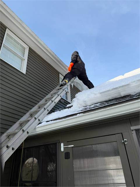 Crew member on a ladder clearing snow and ice from a roof edge