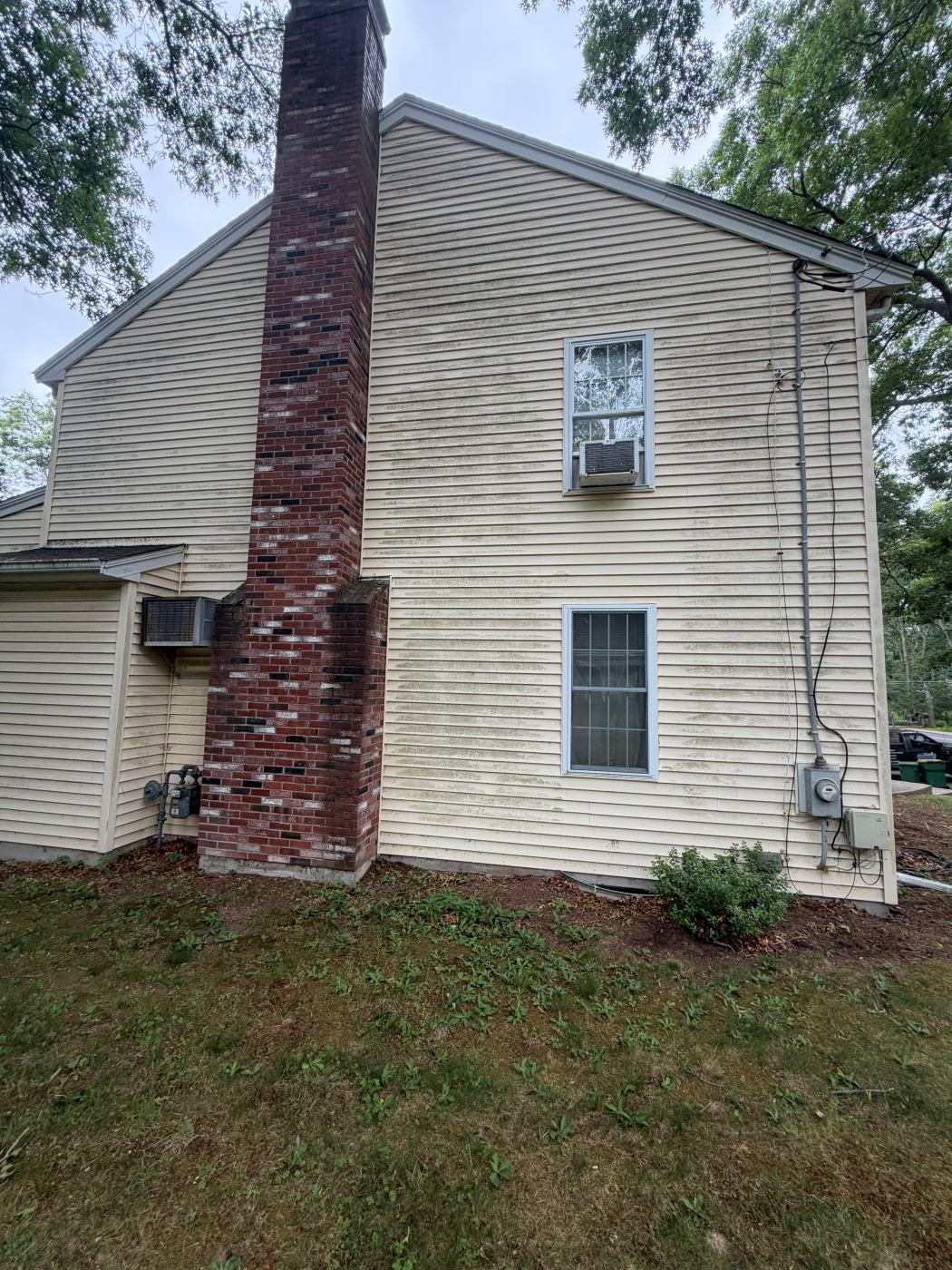 Cream vinyl siding with green mildew streaks beside a brick chimney